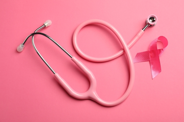 A pink stethoscope against a pink background, beside a pink breast cancer ribbon.