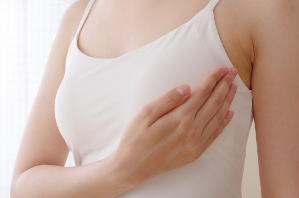 A close-up of a woman in a white tank top performing a self-breast exam.