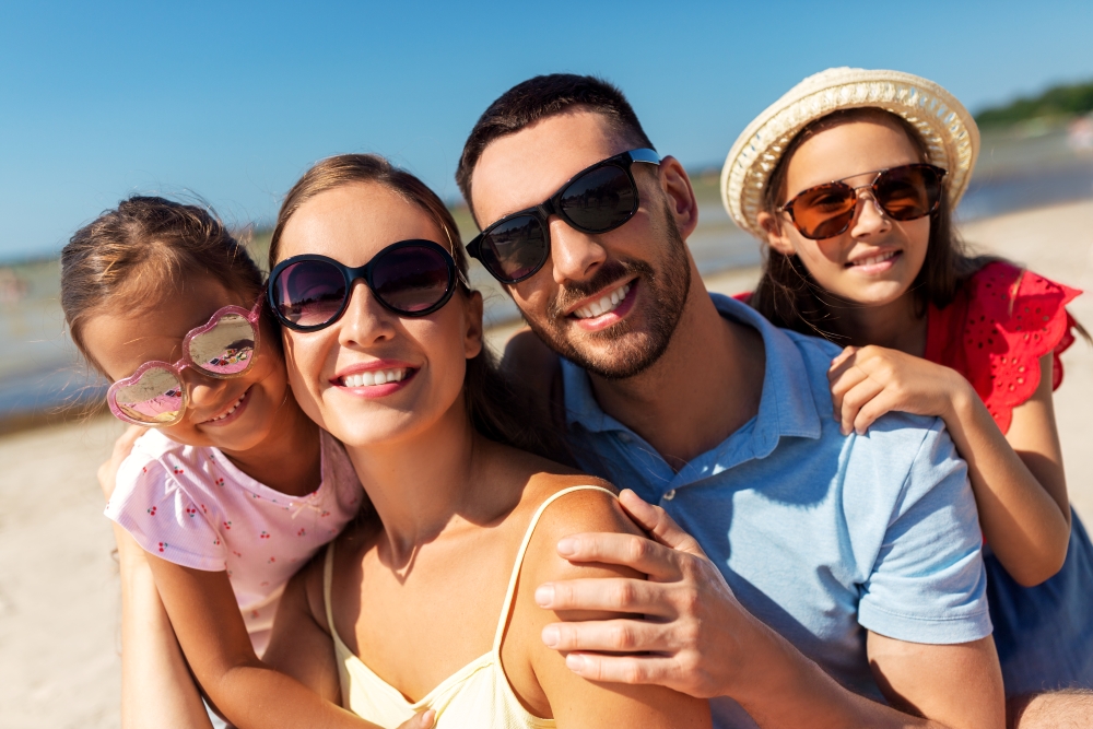 A family of four smile at the camera outdoors, all wearing sunglasses. 