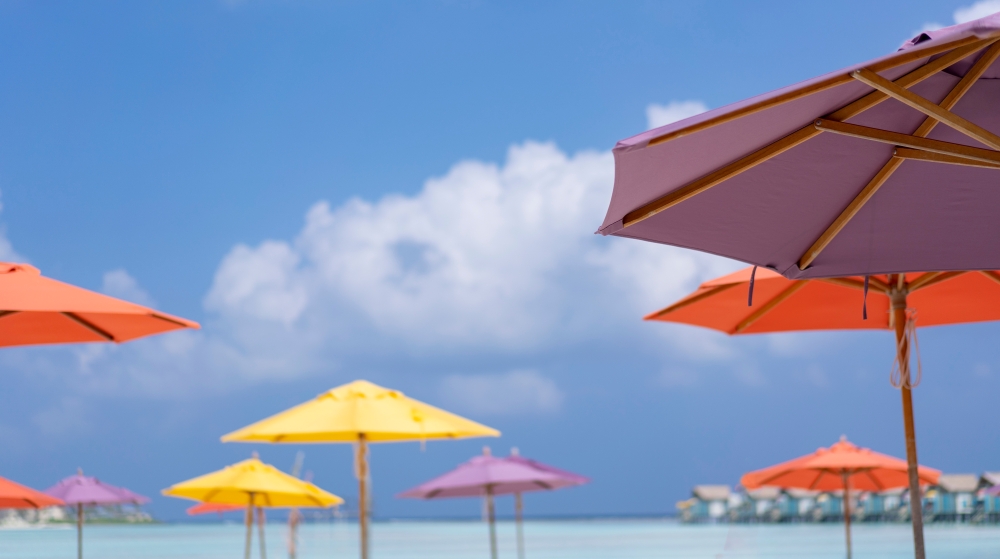 An array of colorful umbrellas on the beach against a blue and cloudy sky. 
