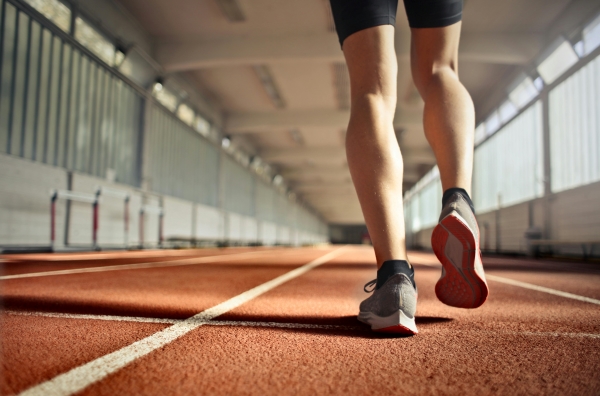 A close-up of a man's legs in running shoes, running along an indoor track.