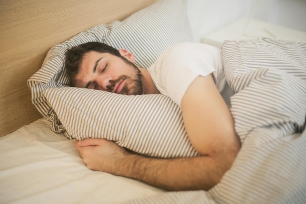 A man in a white t-shirt sleeps on a striped pillow with a matching striped blanket.