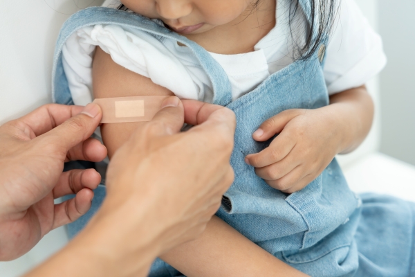 An adult puts a bandage on a baby's arm after giving a vaccine.