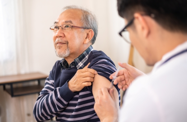 An older man lifts up the sleeve of his shirt as he gets a vaccine.