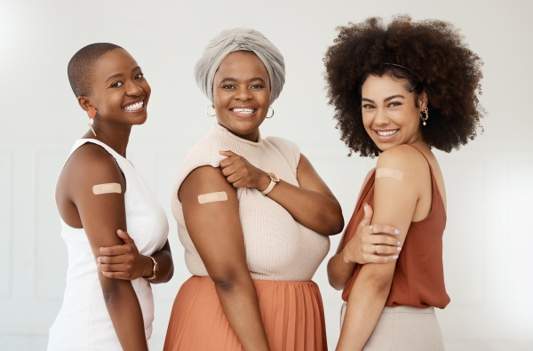 Three smiling women showing bandaids on their upper arm having just received vaccines.