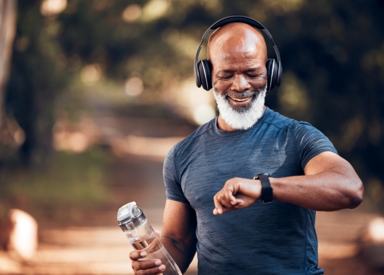 An older man running outdoors with headphones checks his smartwatch.
