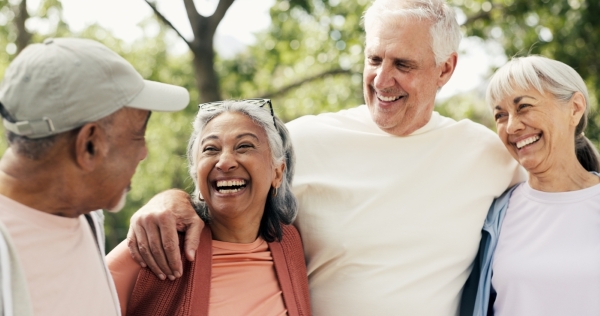 Two older men and two older women outdoors embrace, smiling at one another.
