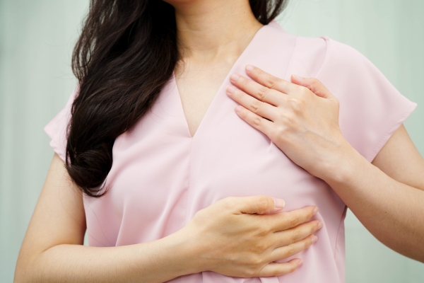 A close-up of a woman in pink scrubs with her hands on her chest.