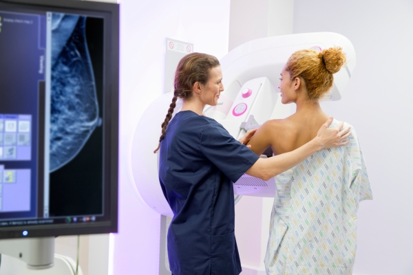 A young woman prioritizes breast cancer screening and receives a mammogram from a nurse in blue scrubs. 