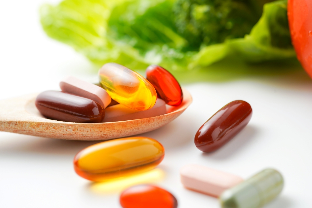 A close-up of vitamin pills on a wooden spoon next to a head of lettuce.