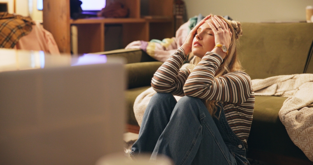 A woman sits on the floor with her head in her hands, surrounded by moving boxes. 