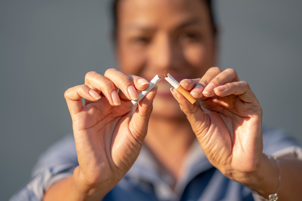 A close-up of a smiling woman holding a cigarette she has ripped in two. 