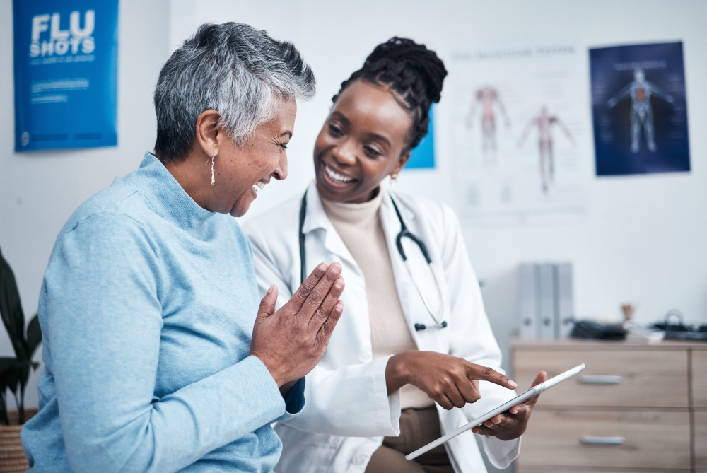 An older woman and a young doctor in a lab coat smile and look at a clipboard together. 