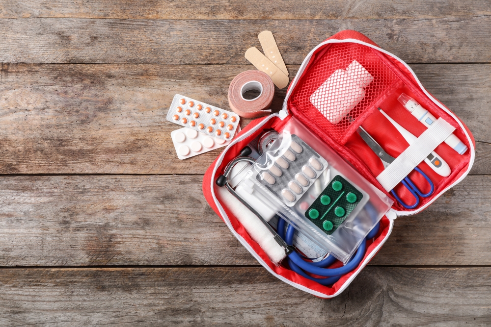 A small medical kit filled with supplies and medication sitting on a wooden background.