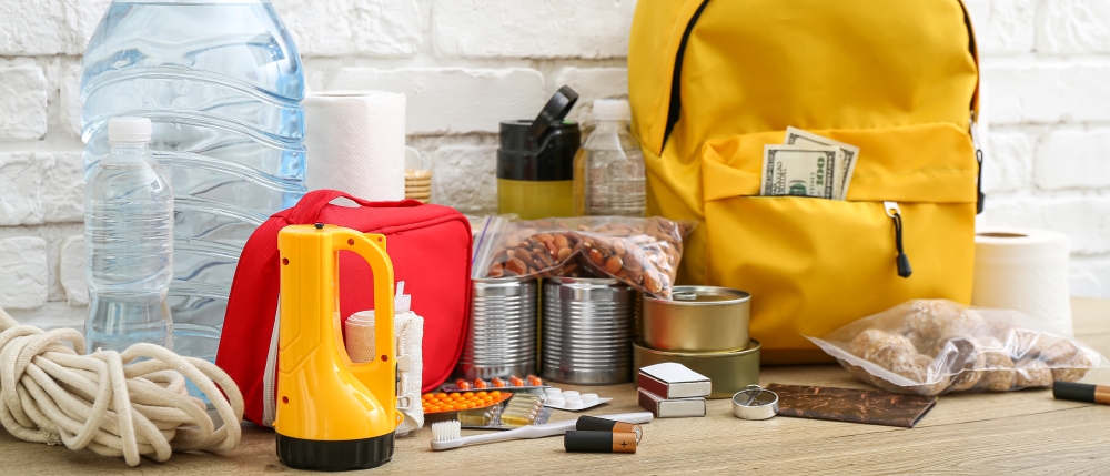 An assortment of supplies, including flashlights, batteries, water, rope, and a yellow backpack.