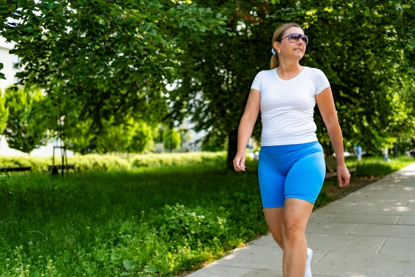 A woman in blue shorts and a white t-shirt goes for a walk outside.